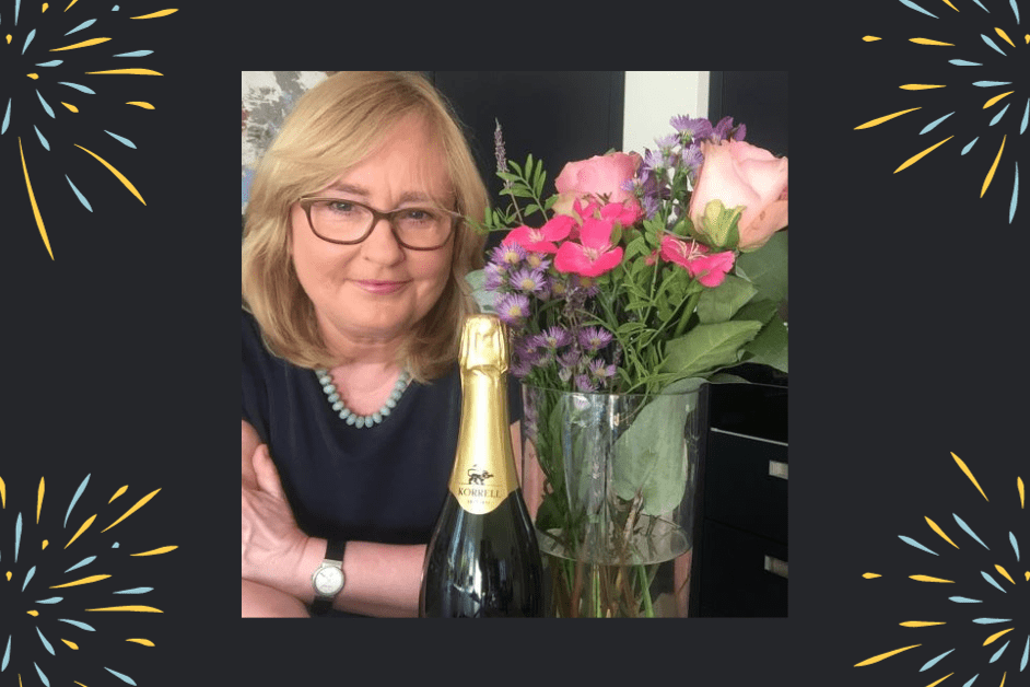 Bettina lächelnd neben einer Flasche Champagner und einem Blumenstrauss