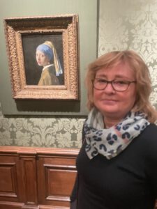 Bettina Walker steht rechts neben dem Gemälde  "Mädchen mit dem Perlenohrring" von Jan Vermeer im Mauritshuis in Den Haag